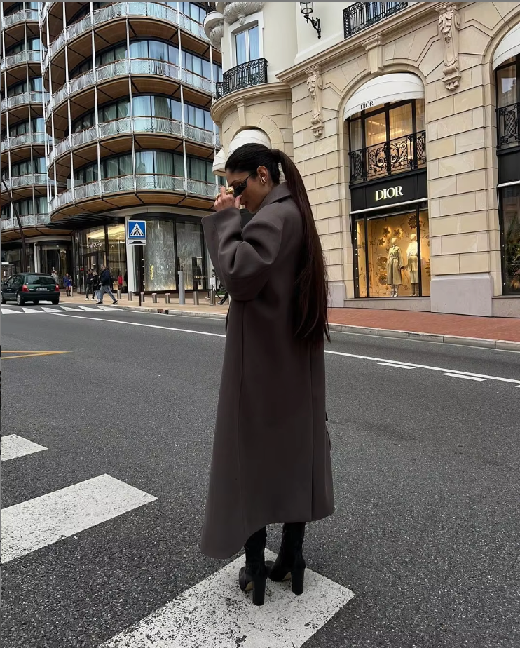 Women's long double-breasted coat worn over layered outfit, showing full-length silhouette