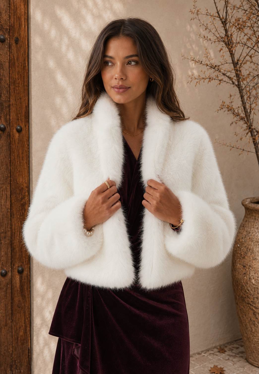 Woman wearing an off-white faux fur jacket with a burgundy skirt, standing indoors