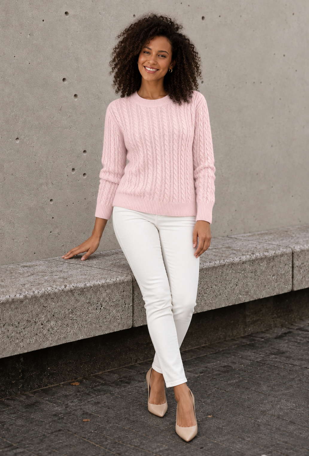 Women's pale pink cable knit sweater with crew neck, full-length view with white jeans and nude heels