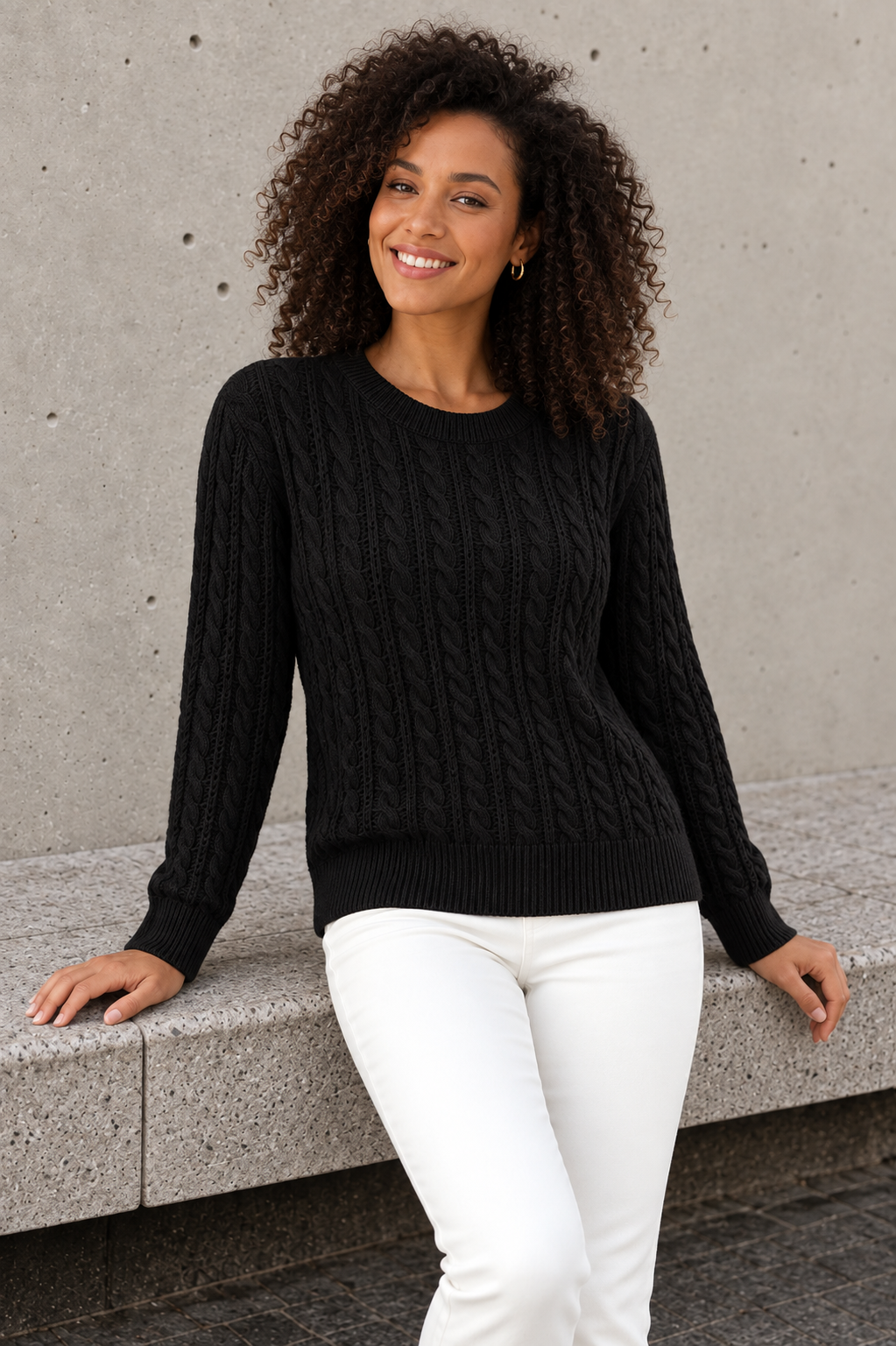 Women's black cable knit sweater with ribbed crew neck, seated front view
